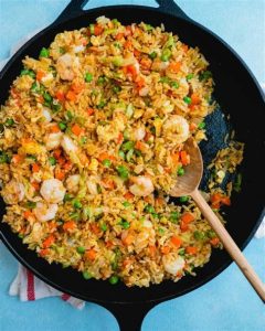 A skillet overflowing with shrimp cauliflower fried rice, showcasing a mix of colorful vegetables and a savory aroma.