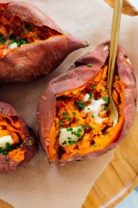 Sweet potatoes filled with spicy chicken, topped with creamy goat cheese and fresh herbs, presented on a rustic plate.