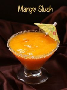 Refreshing spicy mango slush in a glass, garnished with a slice of mango and a hint of chili pepper on top.